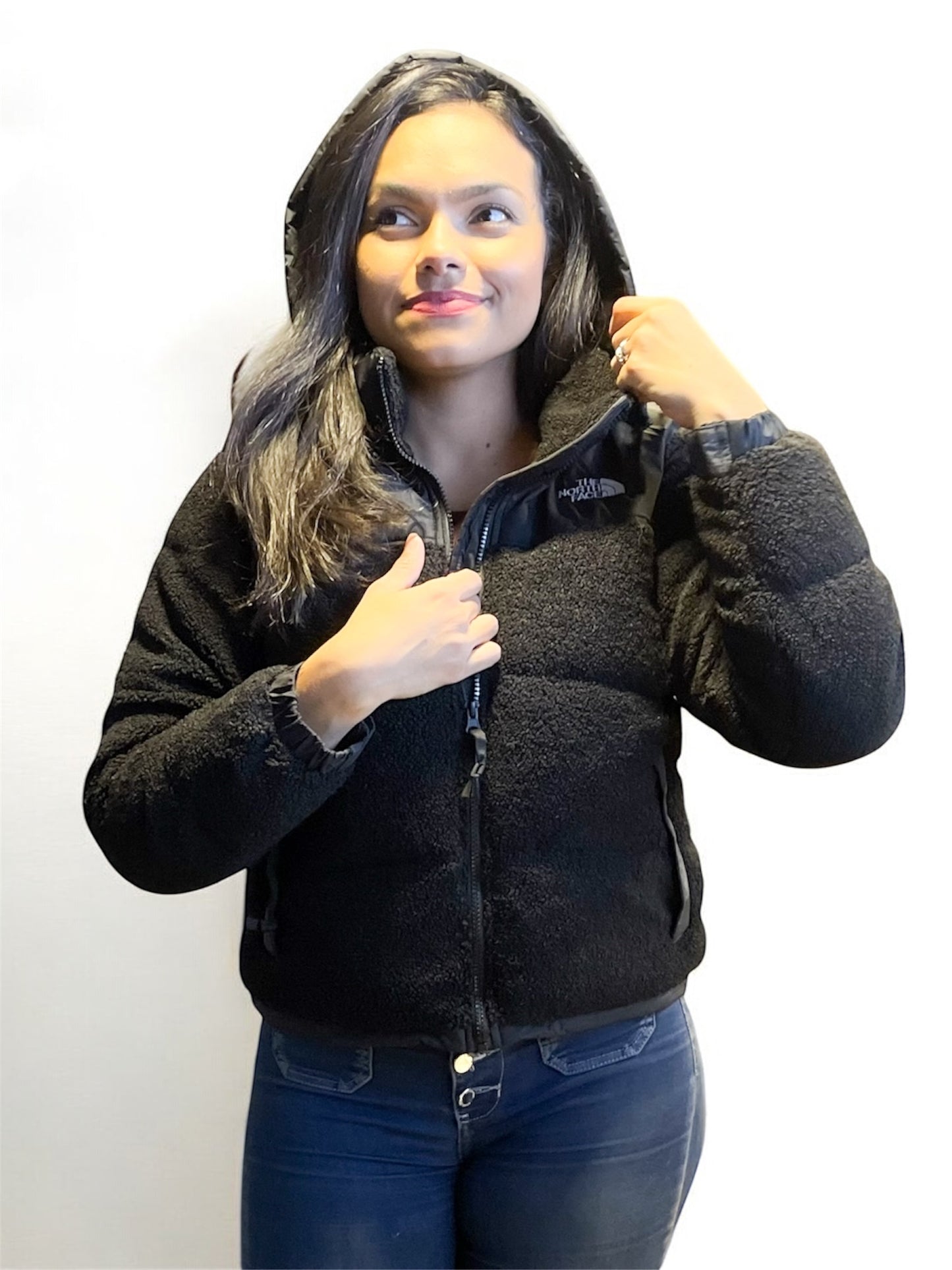 Primer plano de chaqueta teddy negra con capucha y cierre frontal, estilo urbano y abrigado.