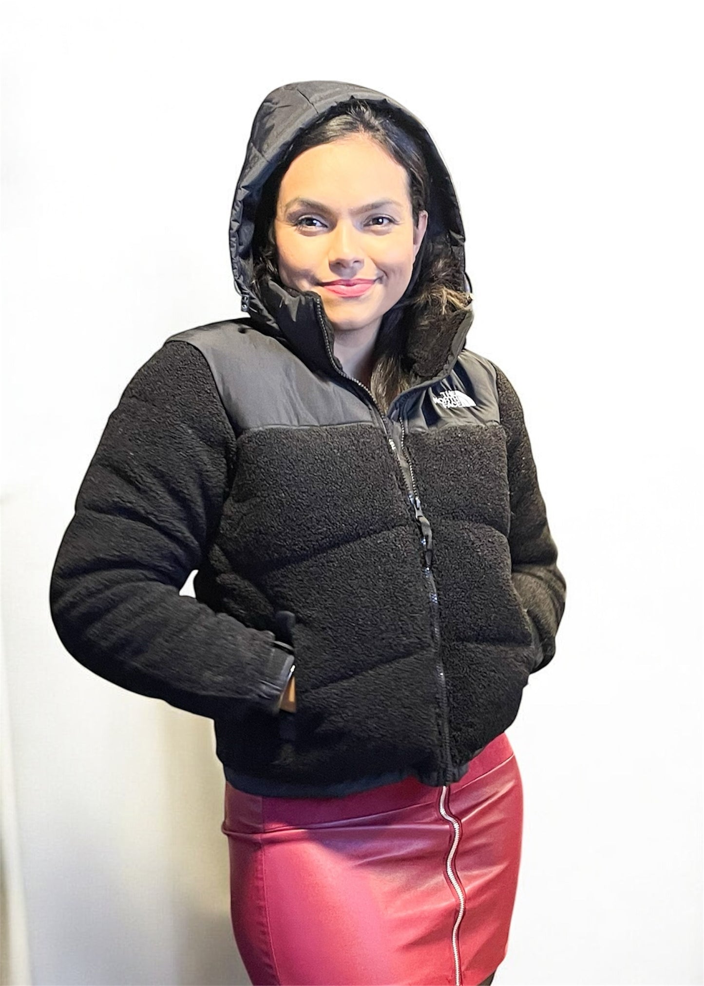 Mujer con capucha puesta y chaqueta teddy negra combinada con falda fucsia de cuero.